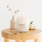 Candle labeled 'Attitude of Gratitude' on a wooden table with decorative items.
