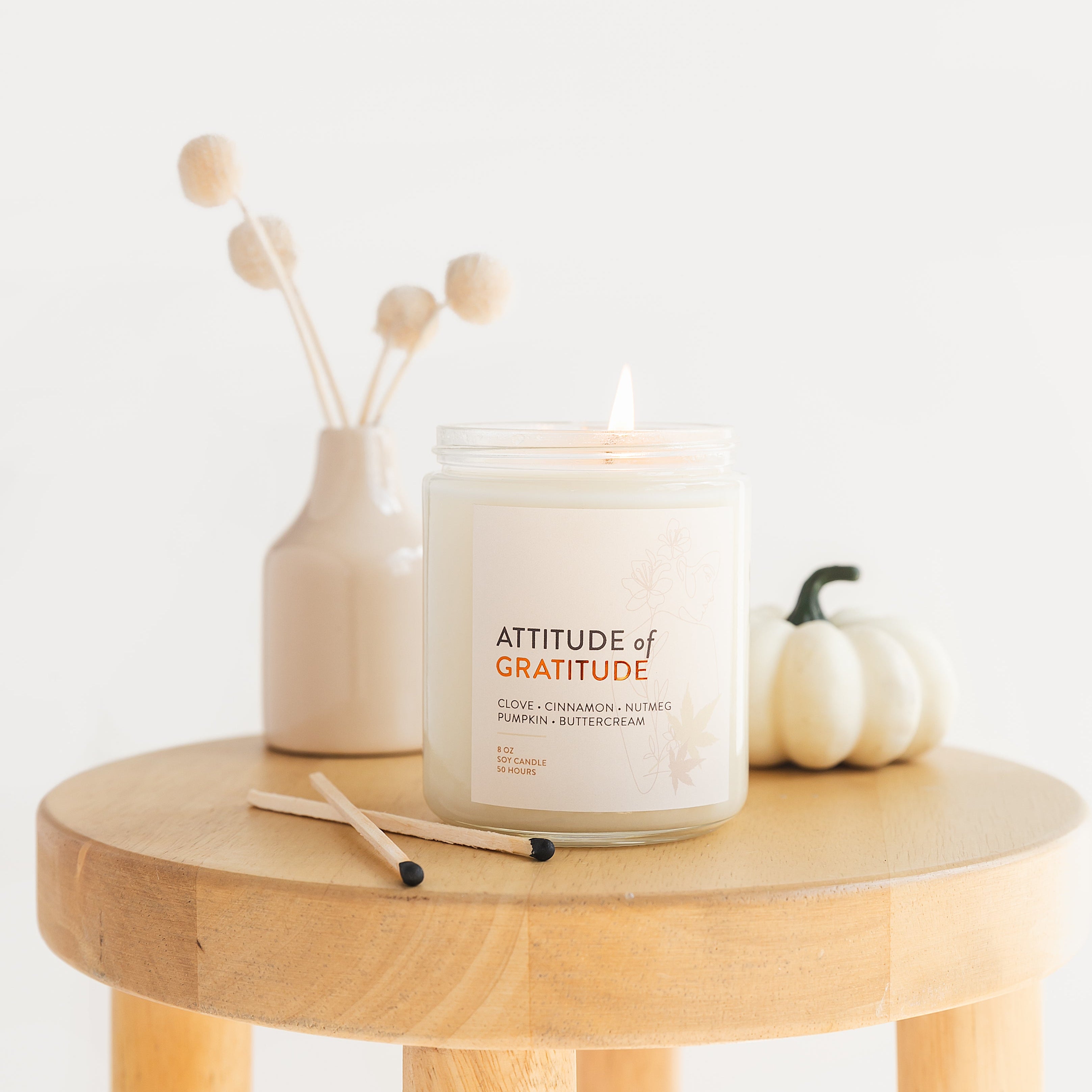 Candle labeled 'Attitude of Gratitude' on a wooden table with decorative items.